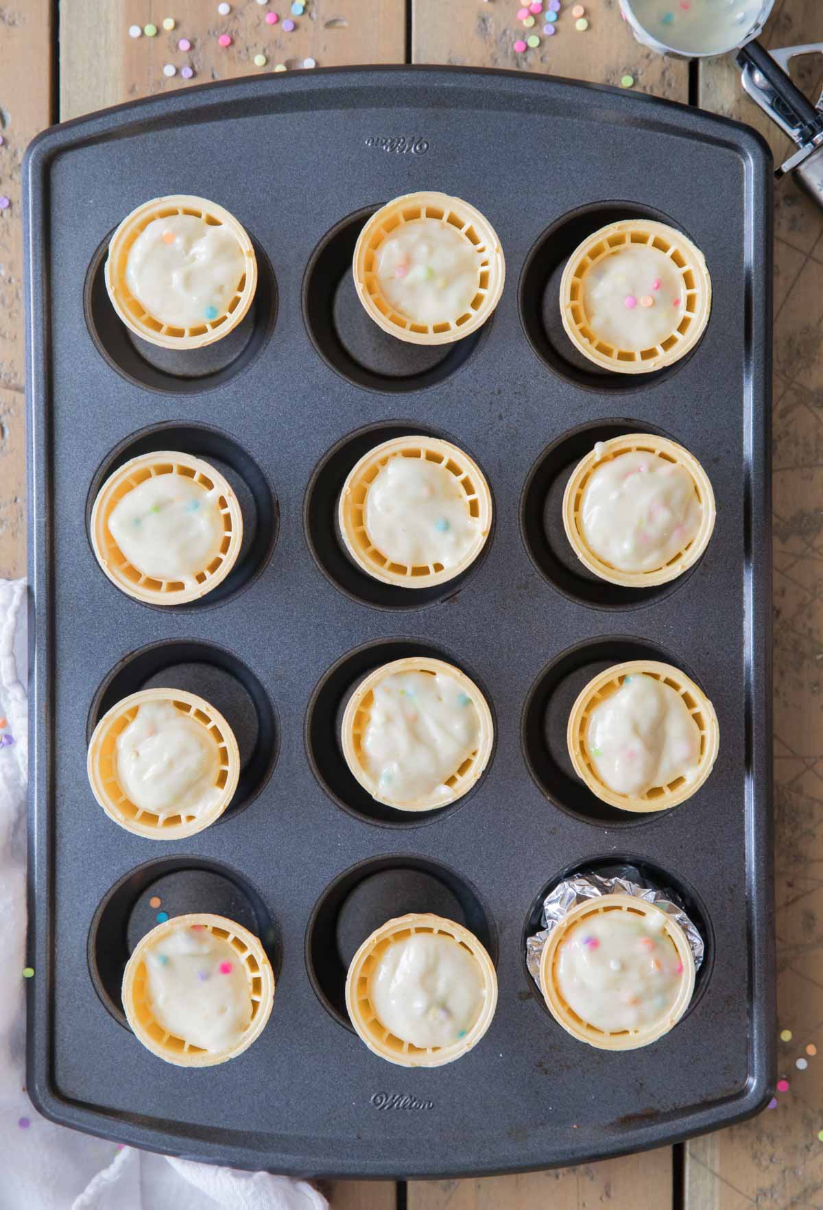 Overhead view of ice cream cones filled with cupcake batter in a cupcake tin.