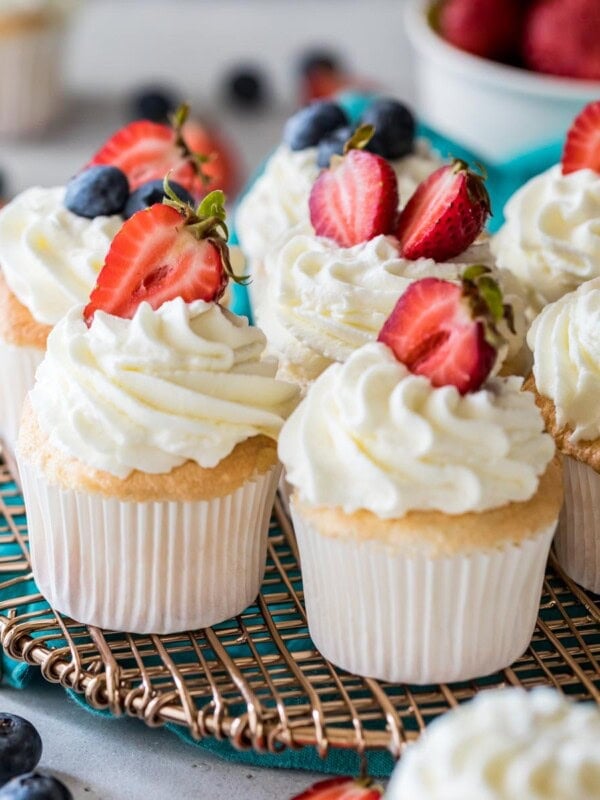 Angel food cupcakes topped with whipped cream and berries on a metal cooling rack.