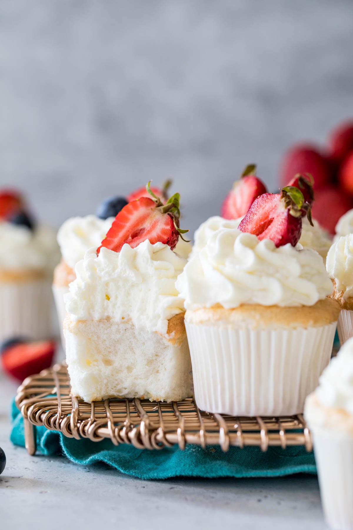 Angel food cupcakes sitting beside each other on a cooling rack, with the left cupcake missing a bite.