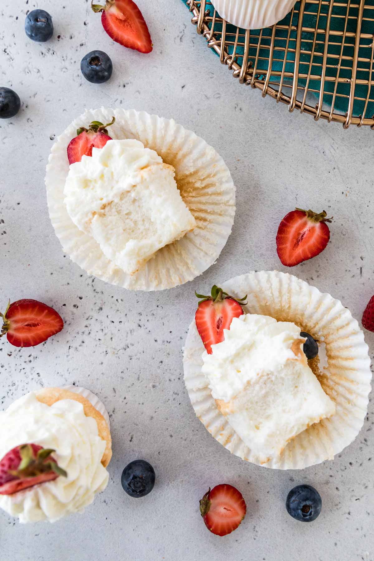 Overhead view of two half eaten cupcakes made from angel food cake batter and topped with whipped cream and strawberries.