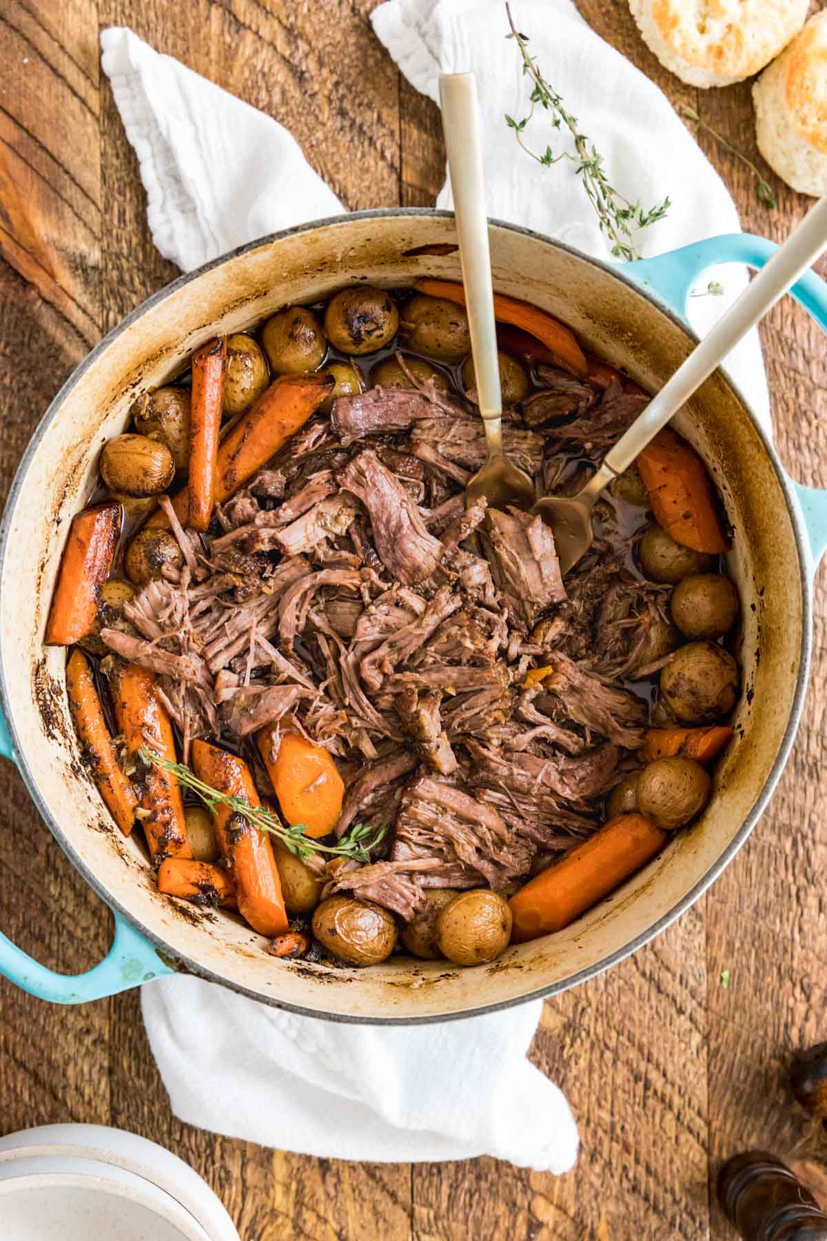 Two forks in a dutch oven with shredded beef, carrots, and baby potatoes inside.