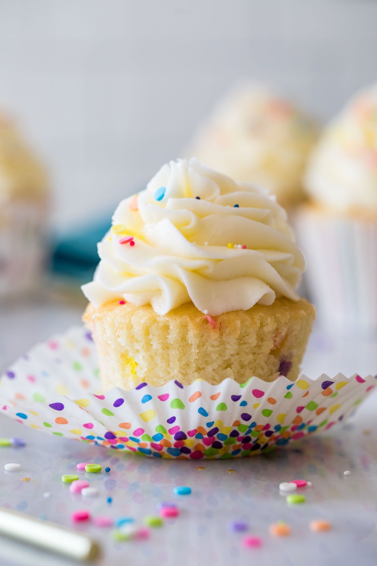 Sprinkle flecked birthday cupcake in a colorful polka dot wrapper that has been unwrapped.