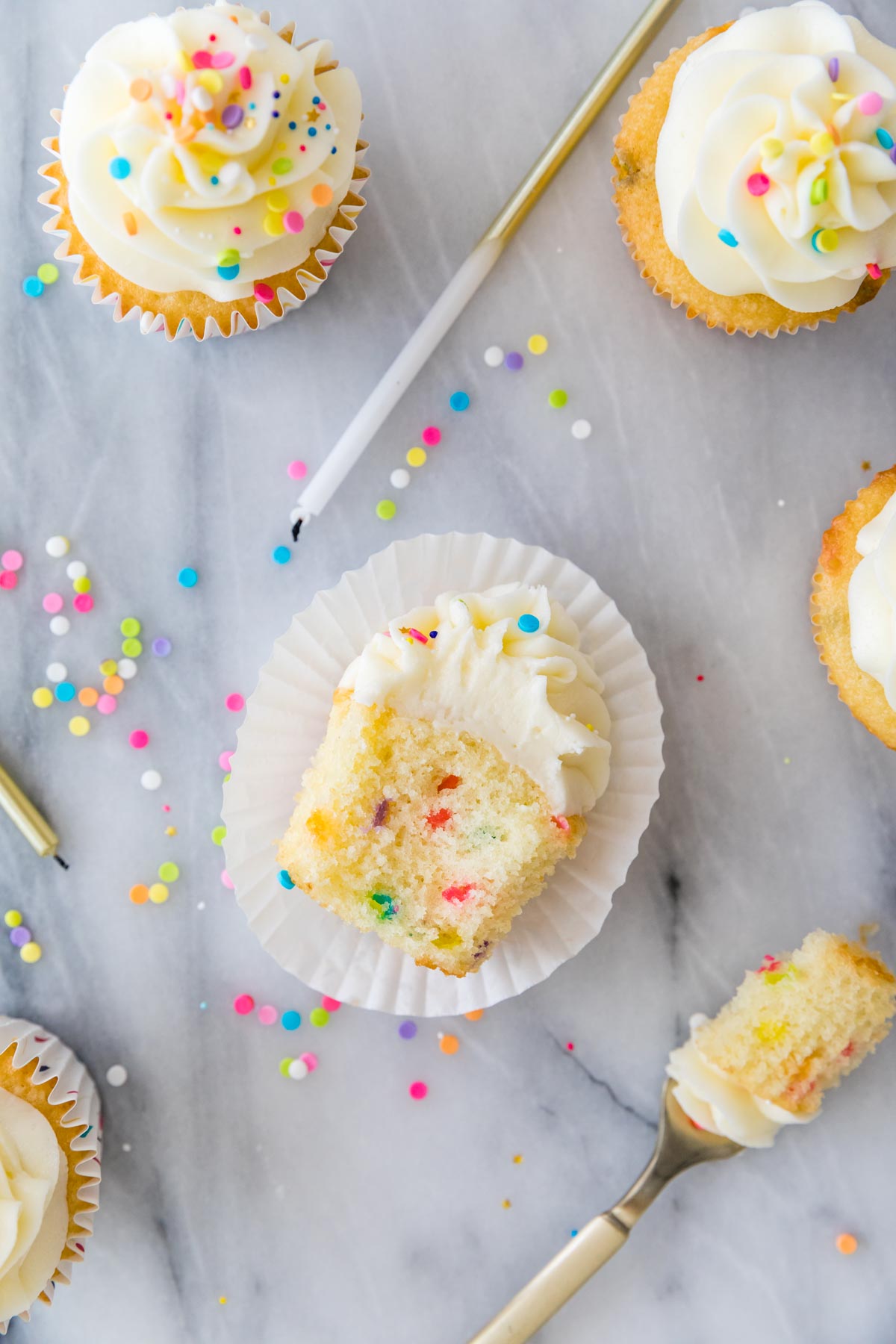 Overhead view of a sprinkle flecked cupcake missing one bite.