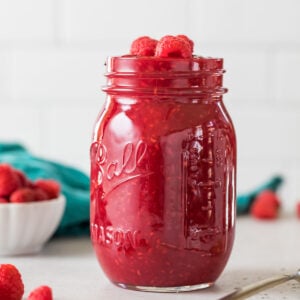 Mason jar of homemade raspberry sauce topped with fresh raspberries.