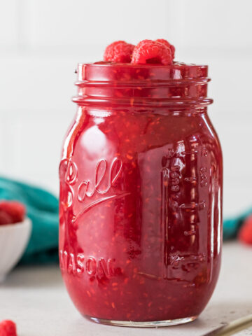 Mason jar of homemade raspberry sauce topped with fresh raspberries.