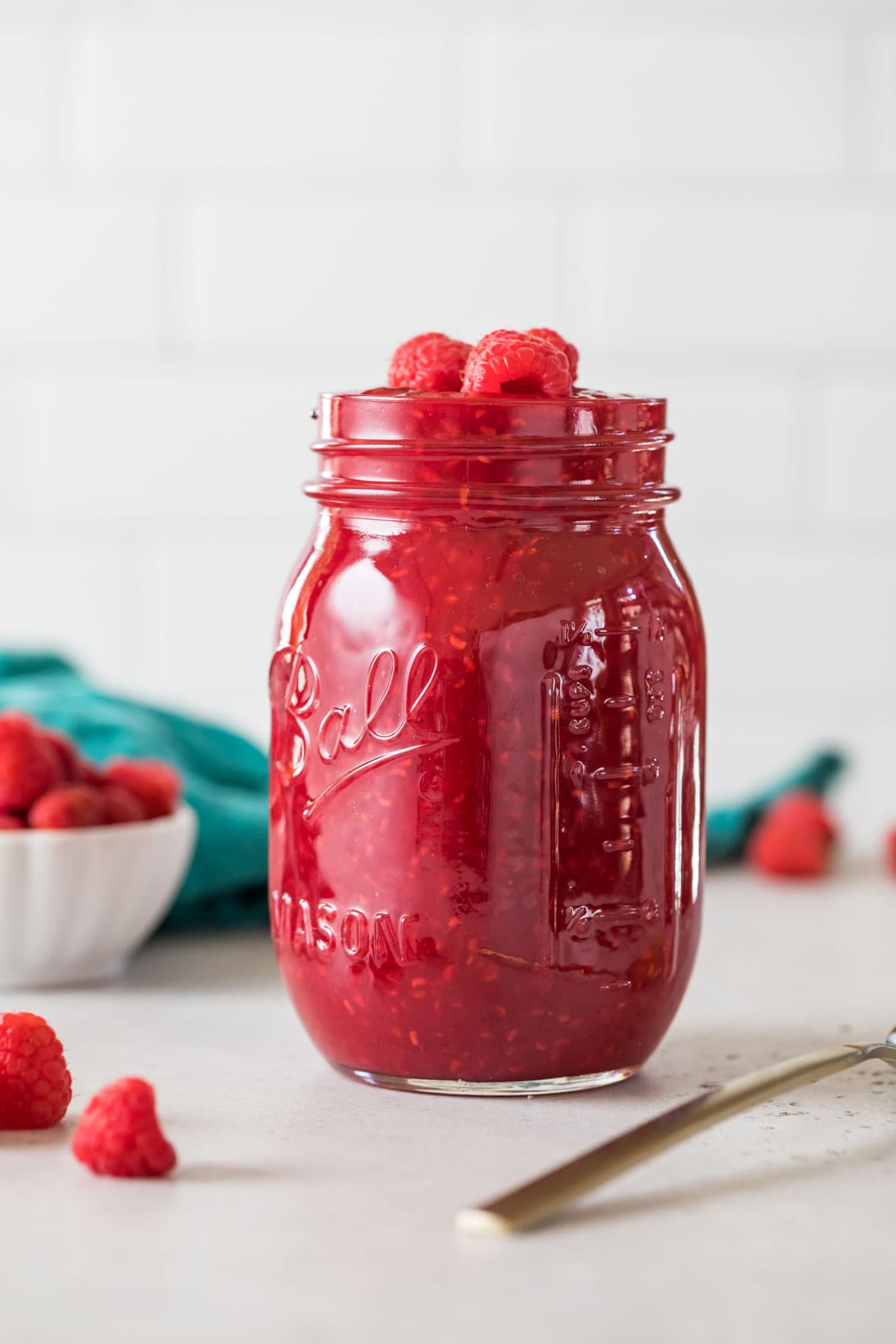 Mason jar of homemade raspberry sauce topped with fresh raspberries.