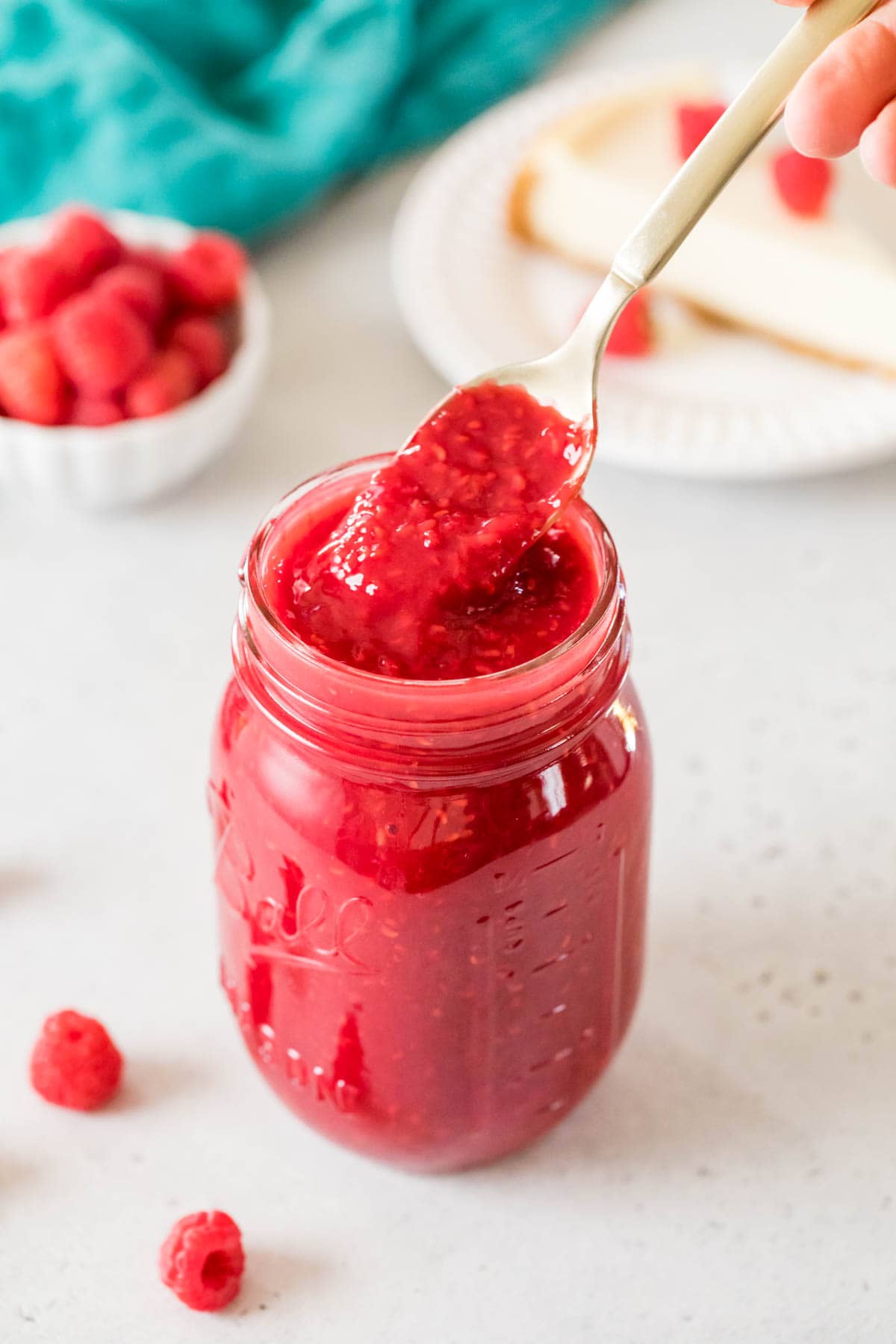 Spoon scooping a red sauce made from raspberries out of a mason jar.