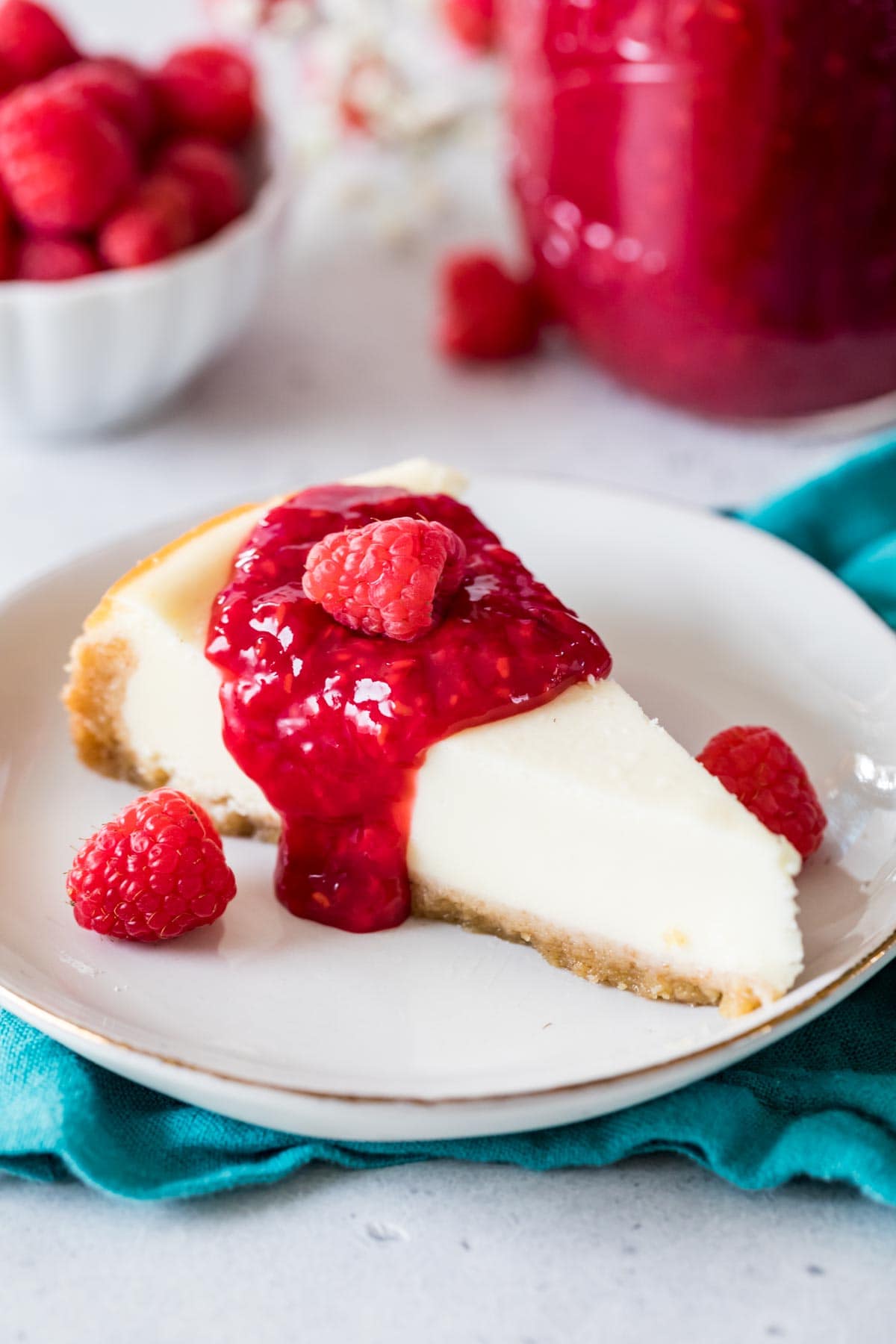 Ein Stück Käsekuchen mit roter Soße und frischen Himbeeren.