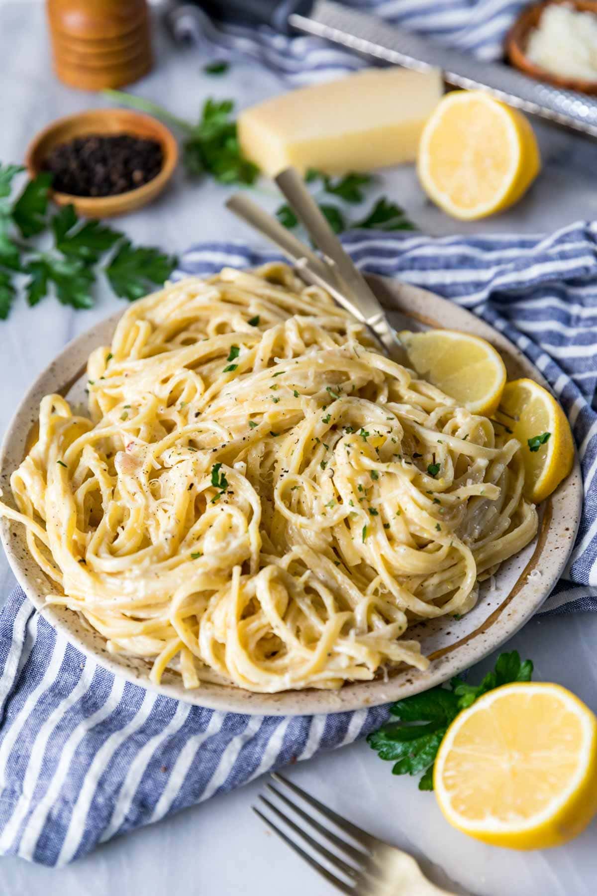 Plate of linguine pasta that's been garnished with parsley and lemon slices.