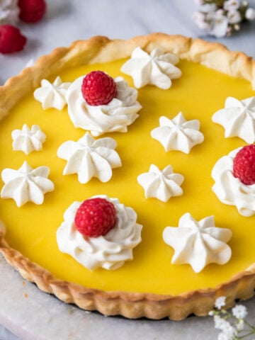 Lemon tart decorated with piped whipped cream and raspberries.