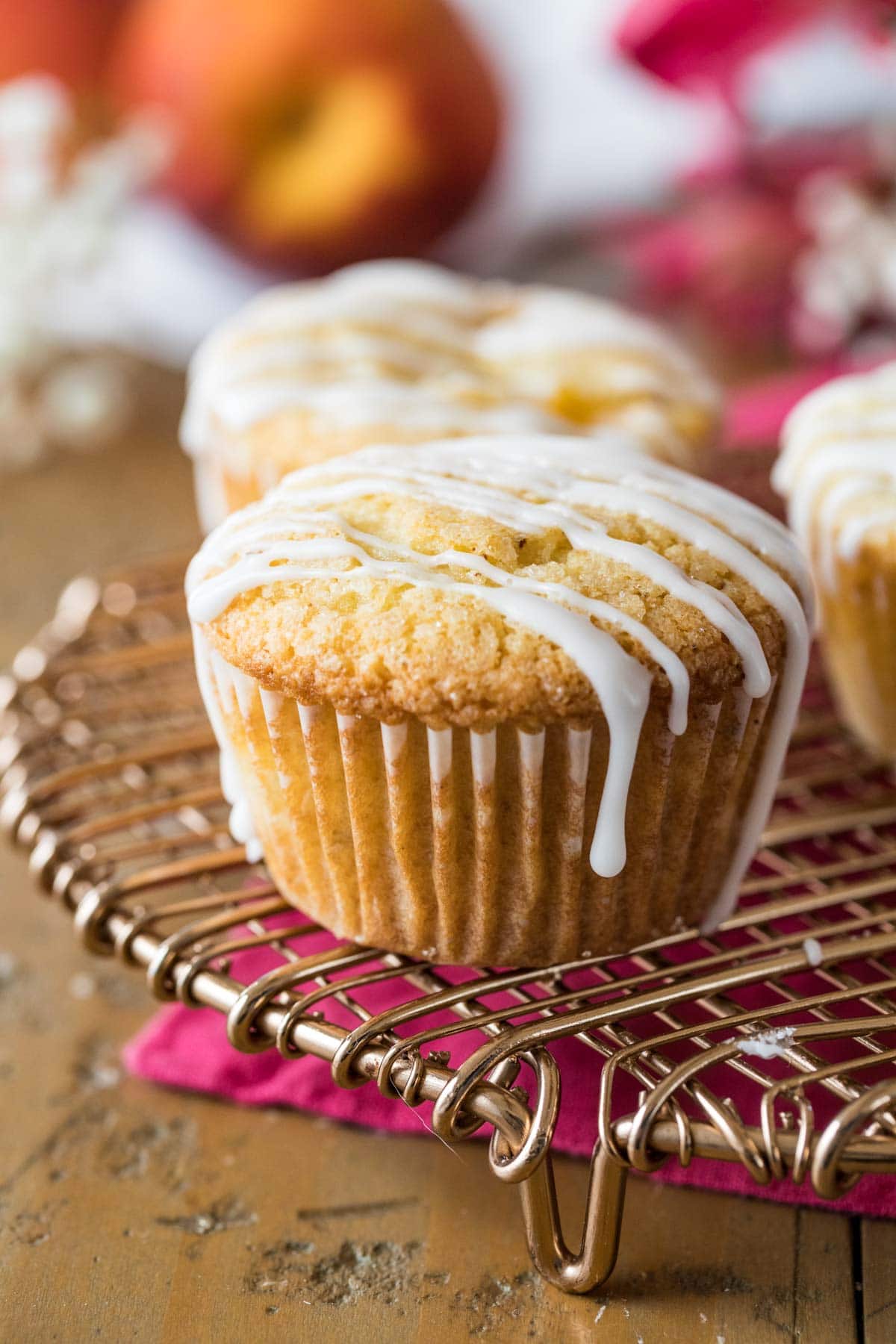 Peach muffins drizzled with vanilla glaze on a cooling rack.