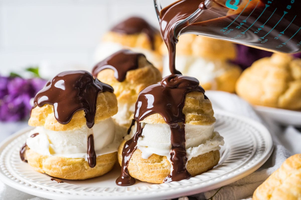 Chocolate ganache being poured over profiteroles.