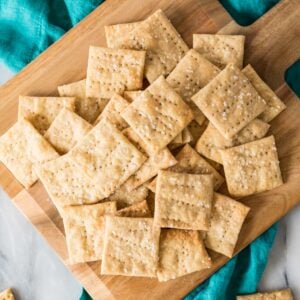 Overhead view of sourdough crackers scattered across a wooden cutting board.