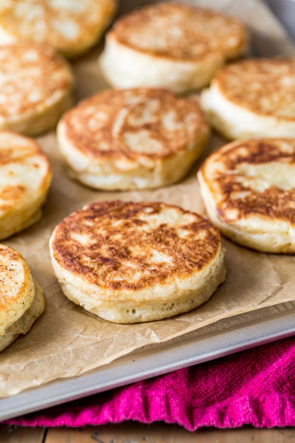 Golden brown English muffins on a parchment lined baking sheet.