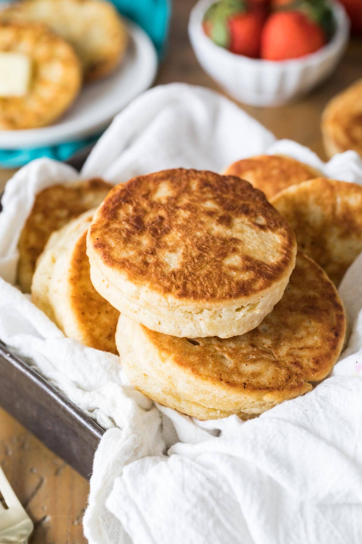 White towel lined pan filled with sourdough English muffins.
