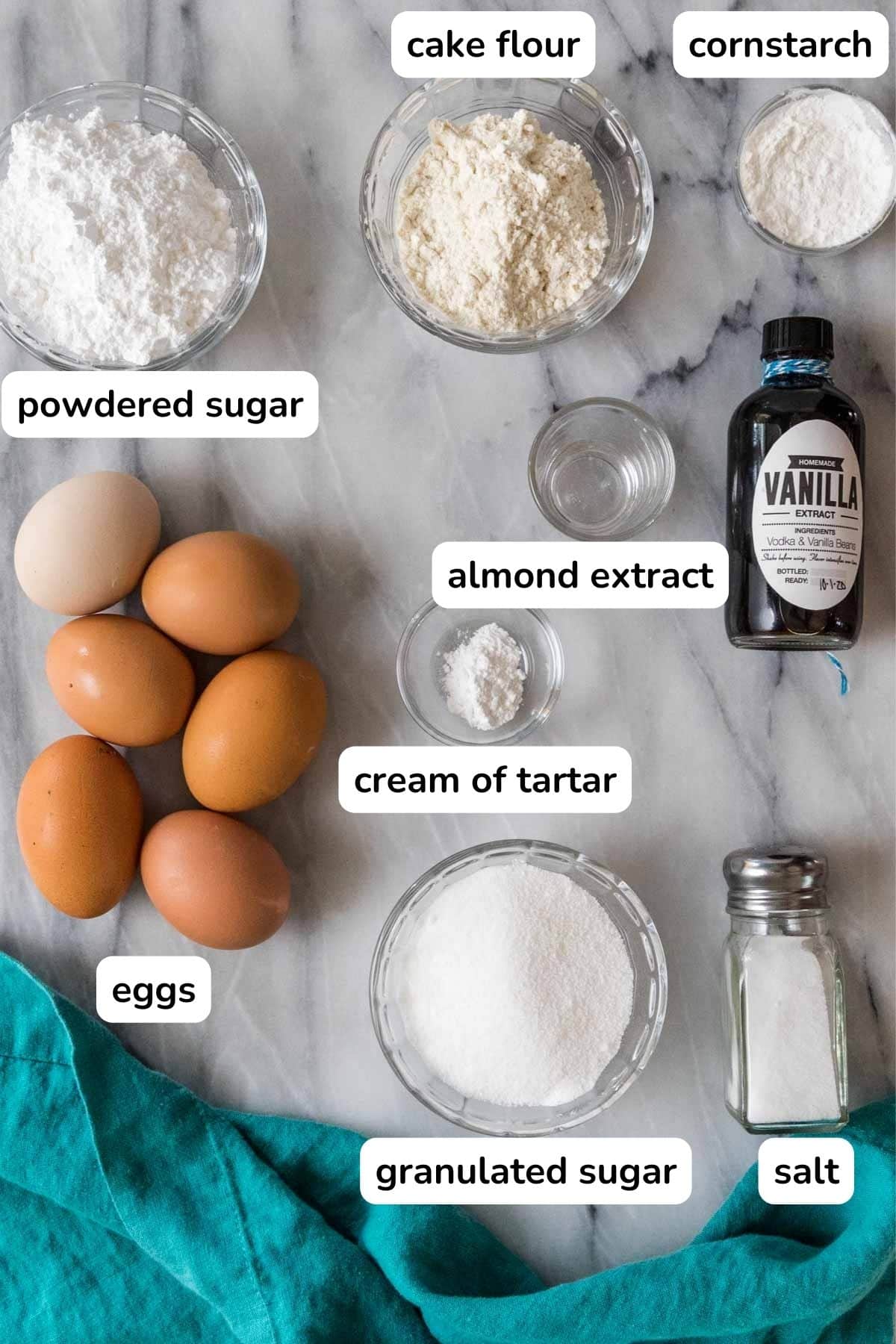 Overhead view of labelled ingredients including eggs, almond extract, cream of tartar, and more.