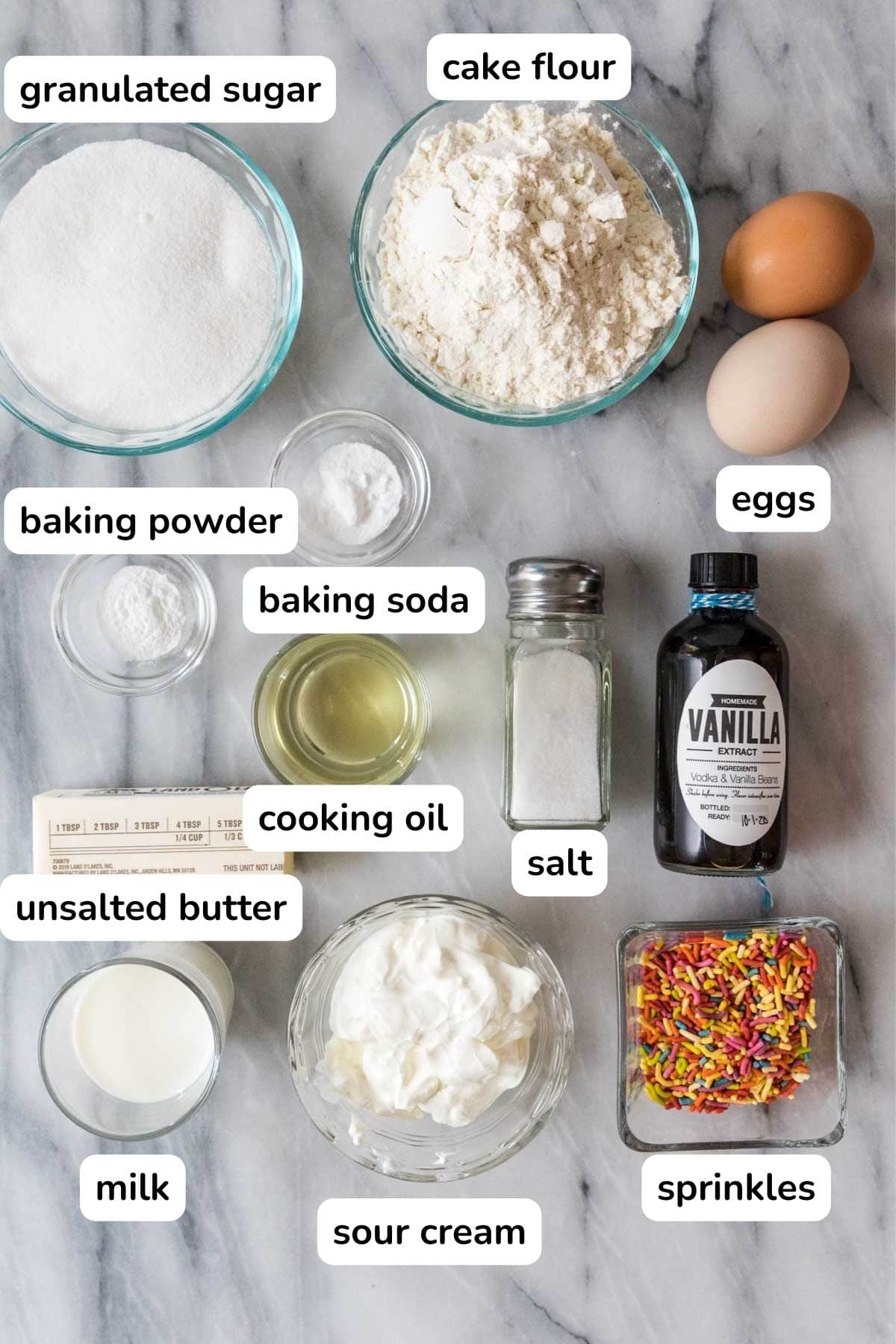Overhead view of labelled ingredients including flour, sugar, eggs, sprinkles, and more.