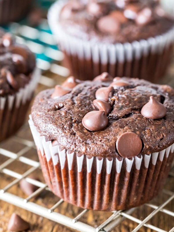 Chocolate zucchini muffins topped with chocolate chips on a metal cooling rack.