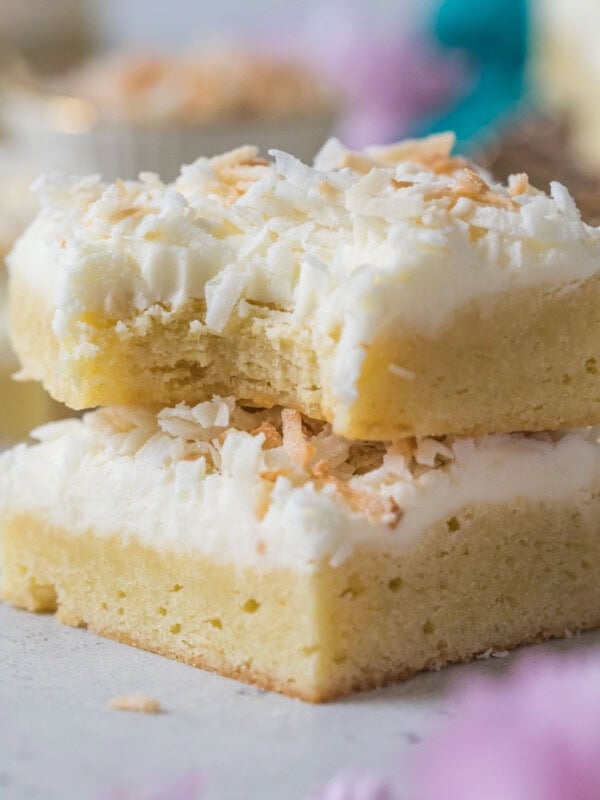 Two coconut cream bars stacked on top of each other, with the top bar missing a bite.