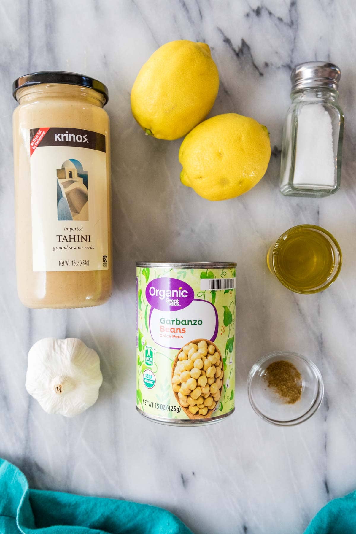 Overhead view of ingredients including tahini, chickpeas, lemons, garlic, and more.