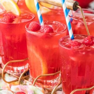 Glasses of homemade raspberry lemonade garnished with fresh berries, lemon slices, and striped straws.