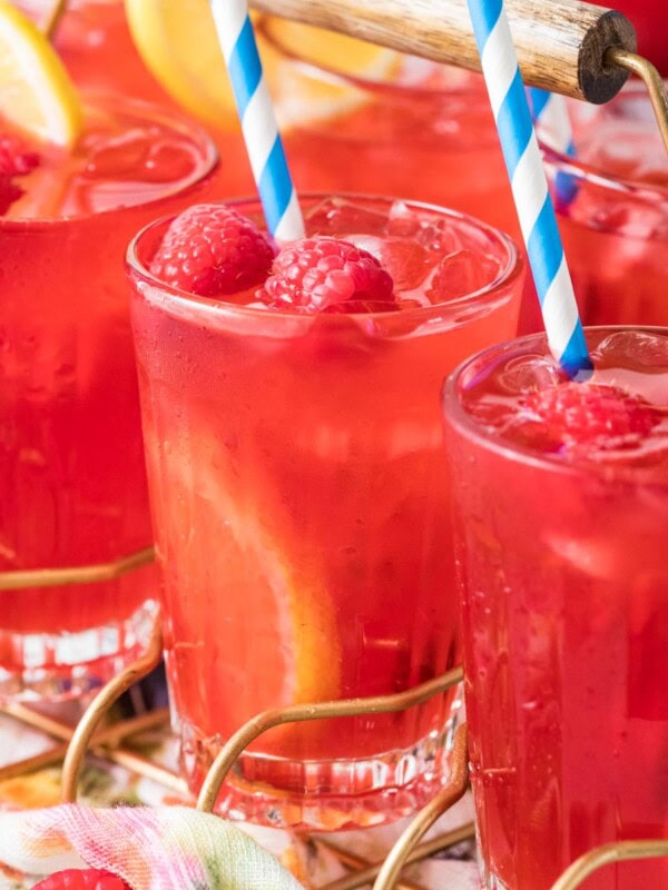 Glasses of homemade raspberry lemonade garnished with fresh berries, lemon slices, and striped straws.