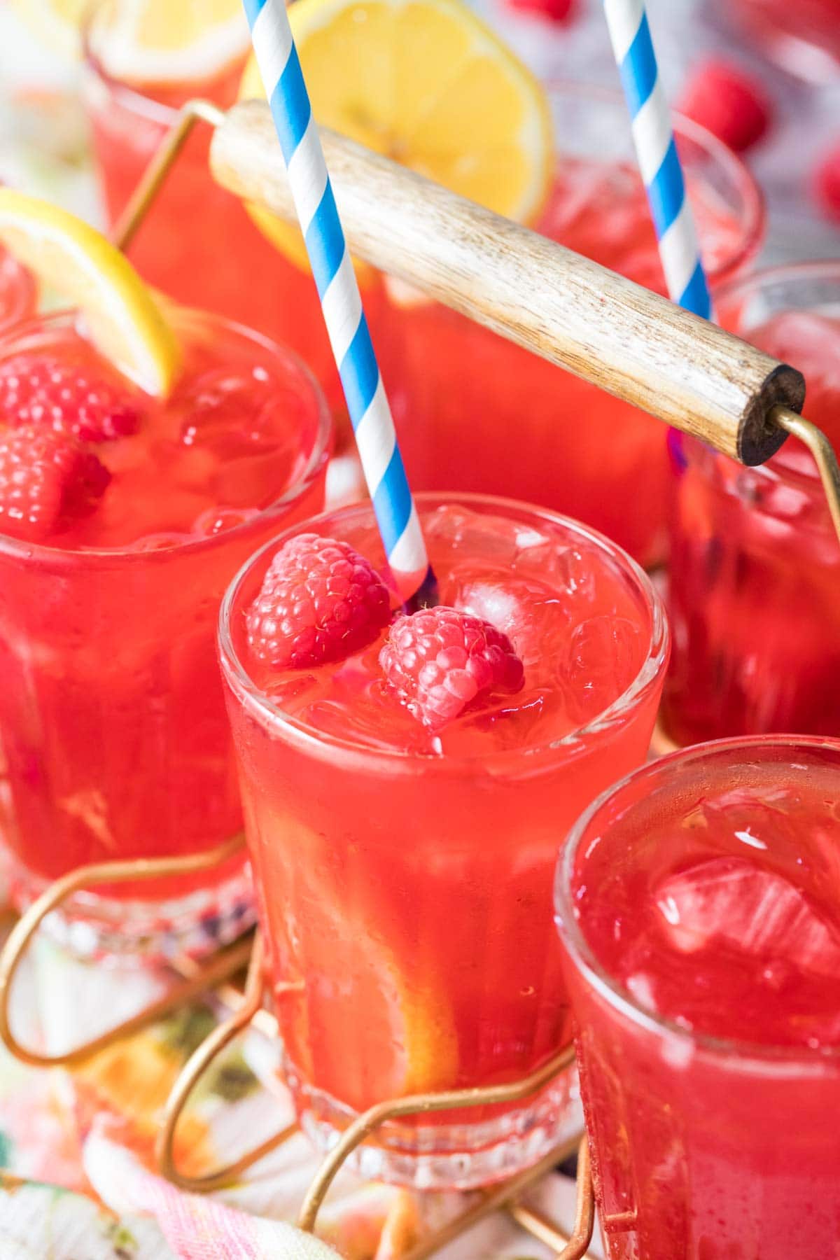 Glasses of red colored lemonade garnished with fresh berries and lemon slices.