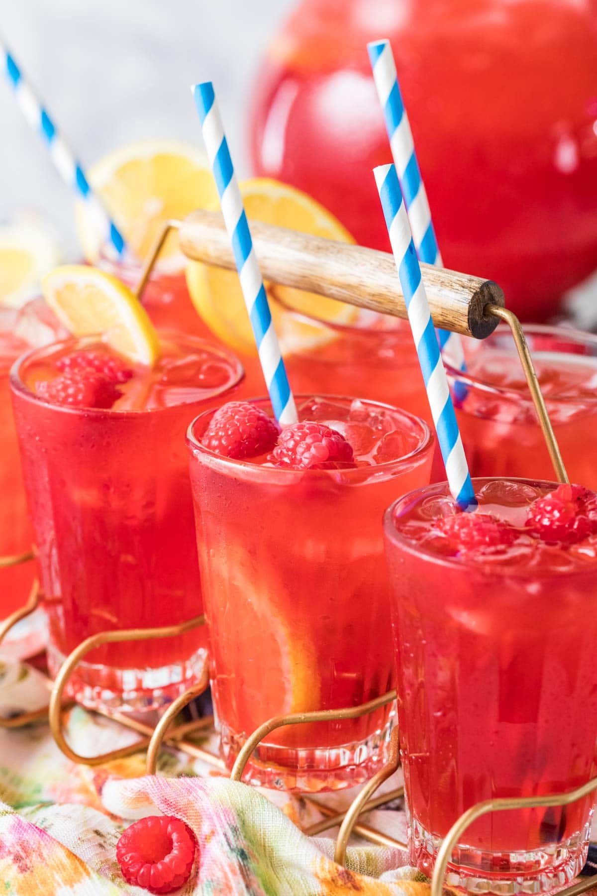 Glasses of homemade raspberry lemonade garnished with fresh berries, lemon slices, and striped straws.