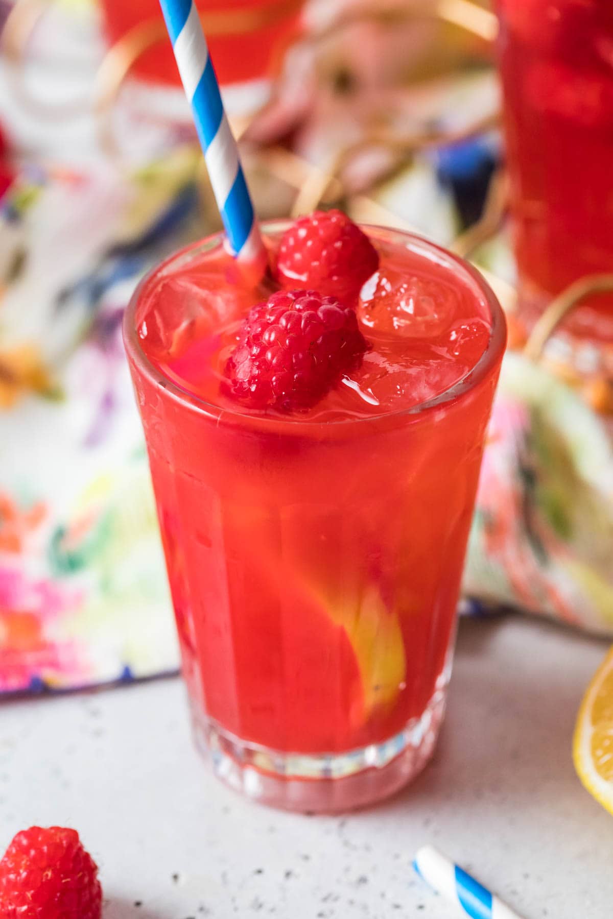 Single glass filled with a red beverage garnished with fresh raspberries.