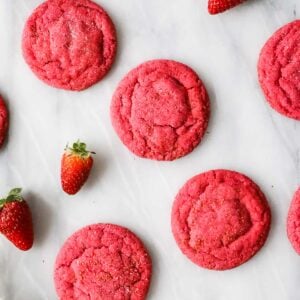 Overhead view of hot pink strawberry cookies on a white marble countertop.