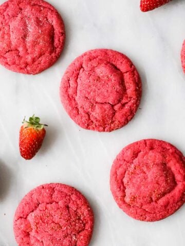 Overhead view of hot pink strawberry cookies on a white marble countertop.
