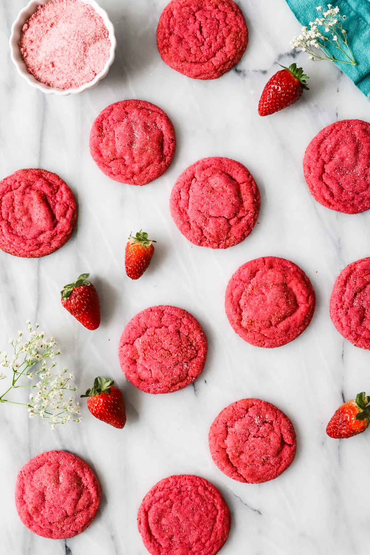 Overhead view of hot pink strawberry cookies on a white marble countertop.