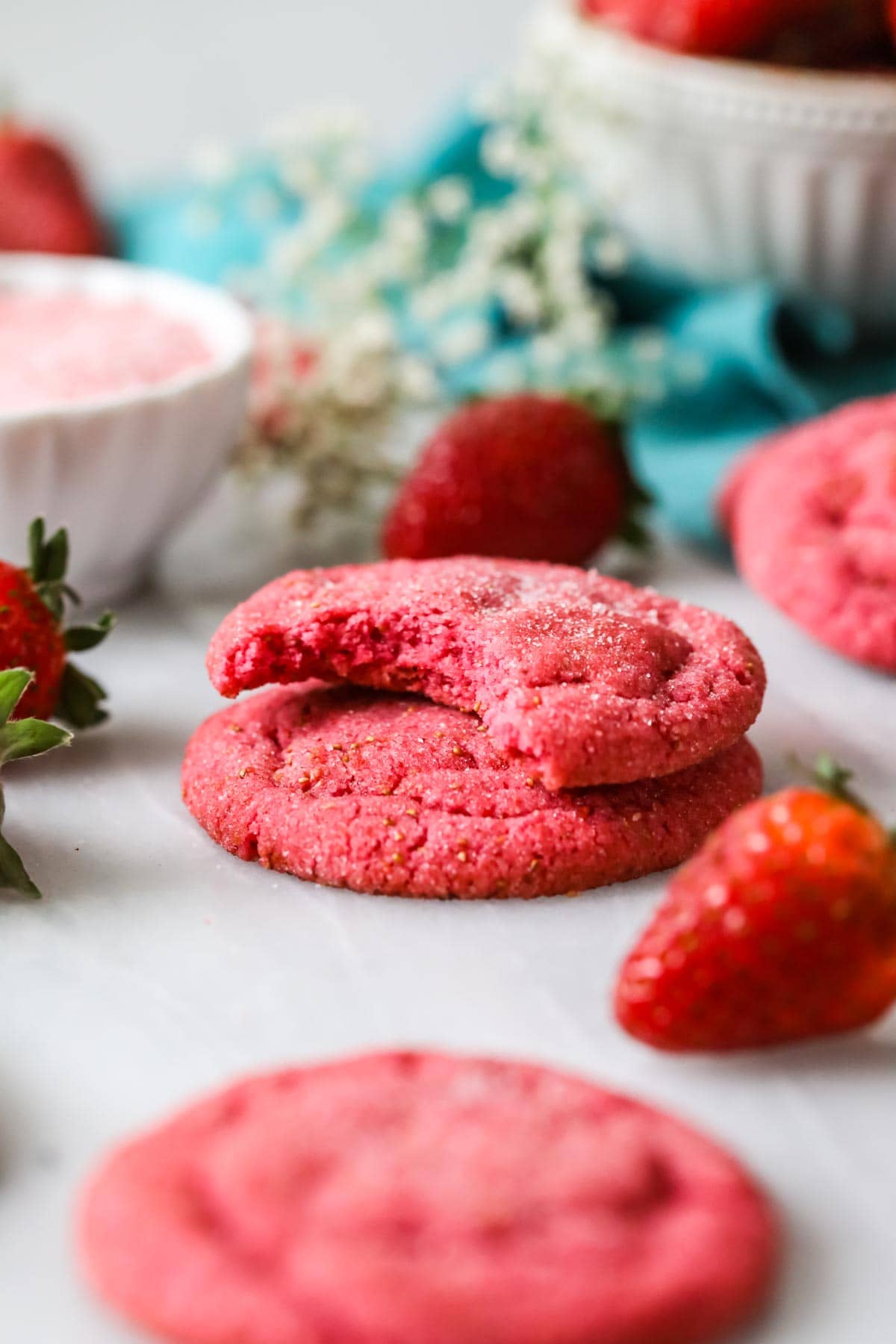 Two strawberry cookies stacked on top of each other with the top cookie missing a bite.