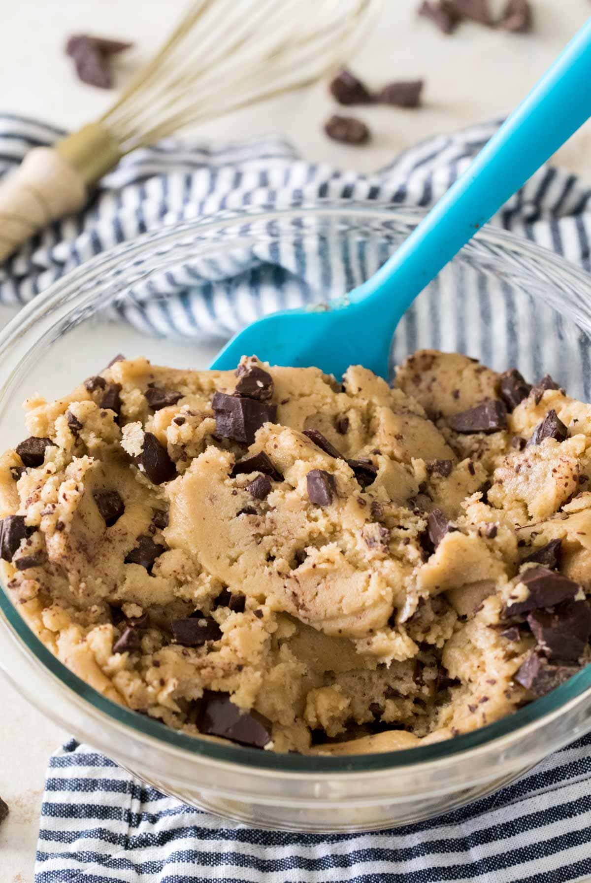Bowl of chocolate chip cookie dough with a blue silicone spatula resting in it.