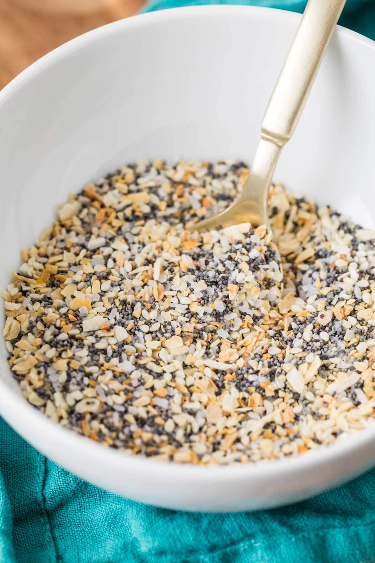 Spoon scooping everything bagel seasoning out of a white bowl.