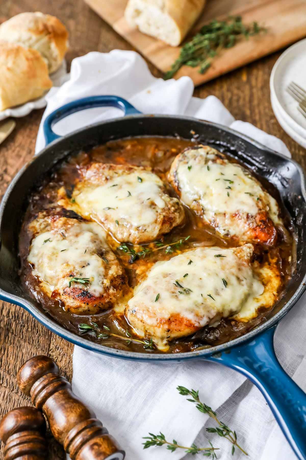 Cast iron skillet with chicken breasts in an onion sauce topped with melted cheese.