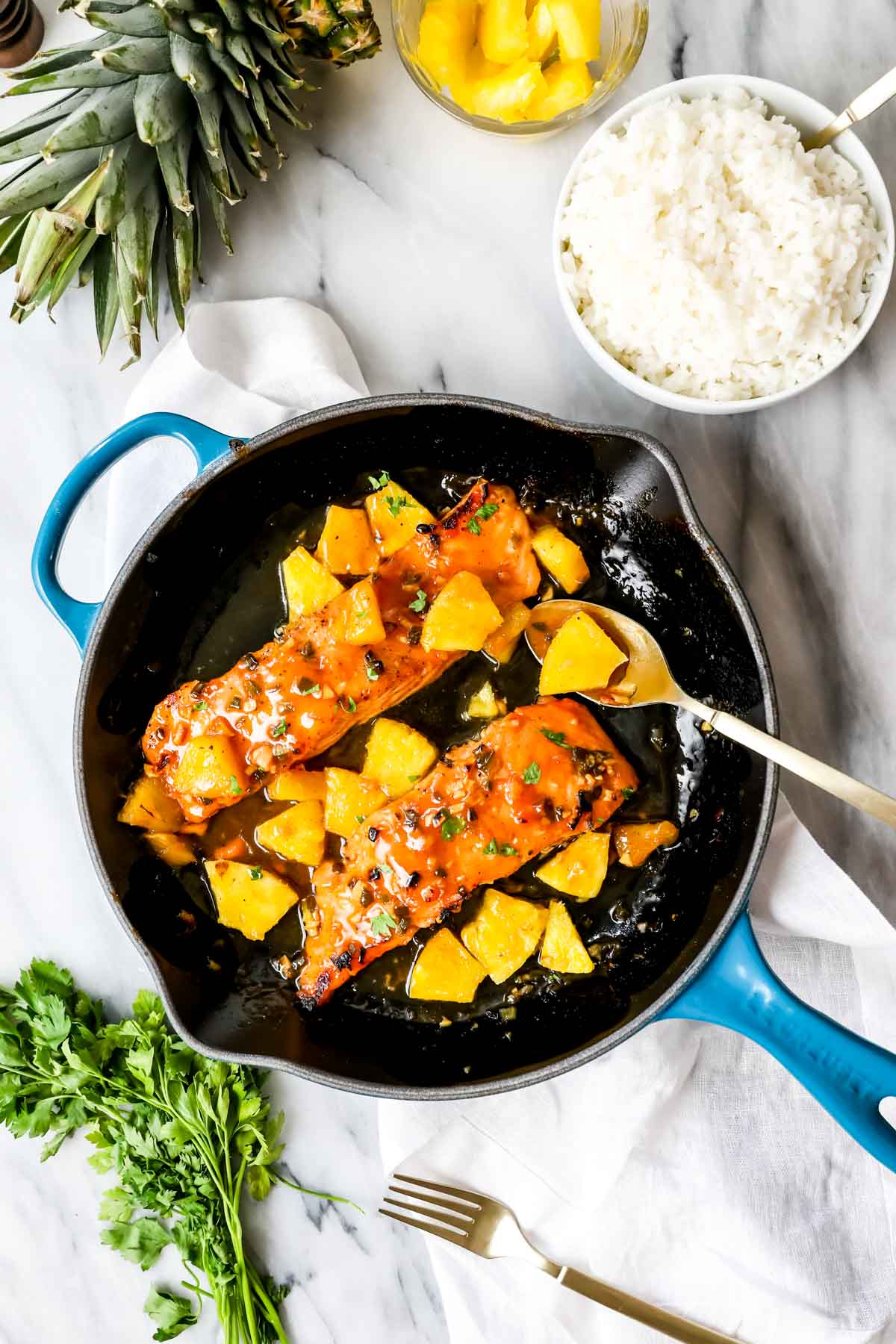 Overhead view of a skillet of glazed salmon topped with pineapple pieces.
