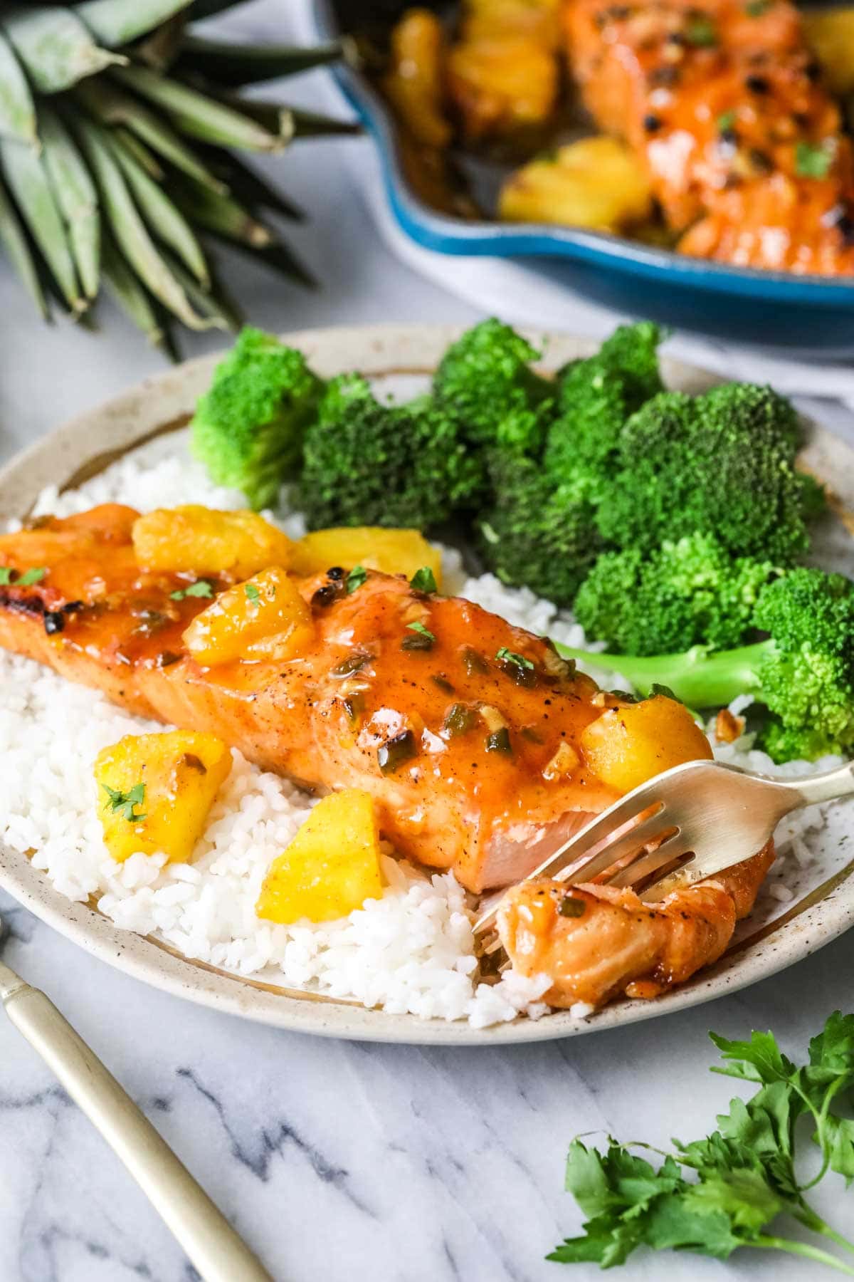 Fork cutting into maple glazed salmon served on a bed of rice with a side of broccoli.