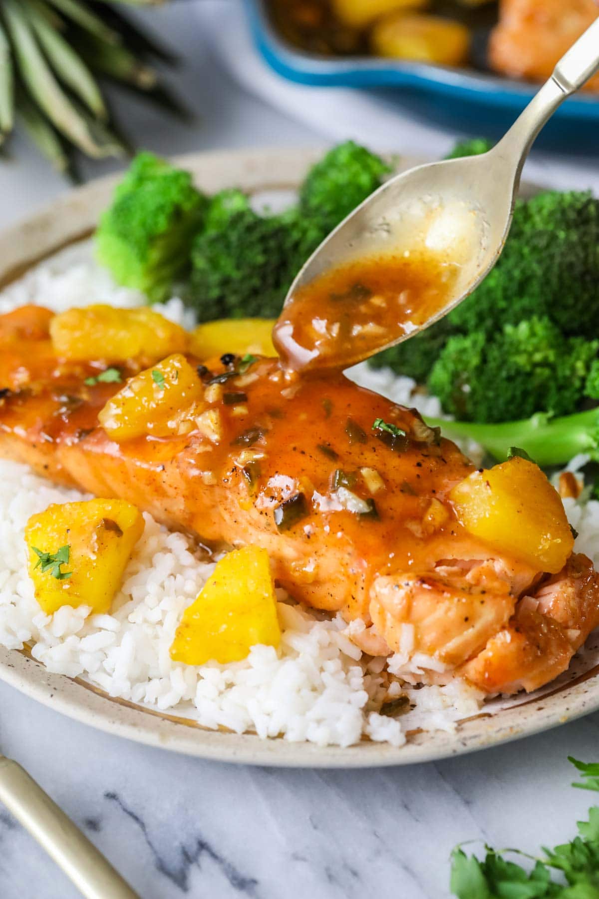 Sauce being poured over a piece of salmon topped with pineapple on a bed of white rice.