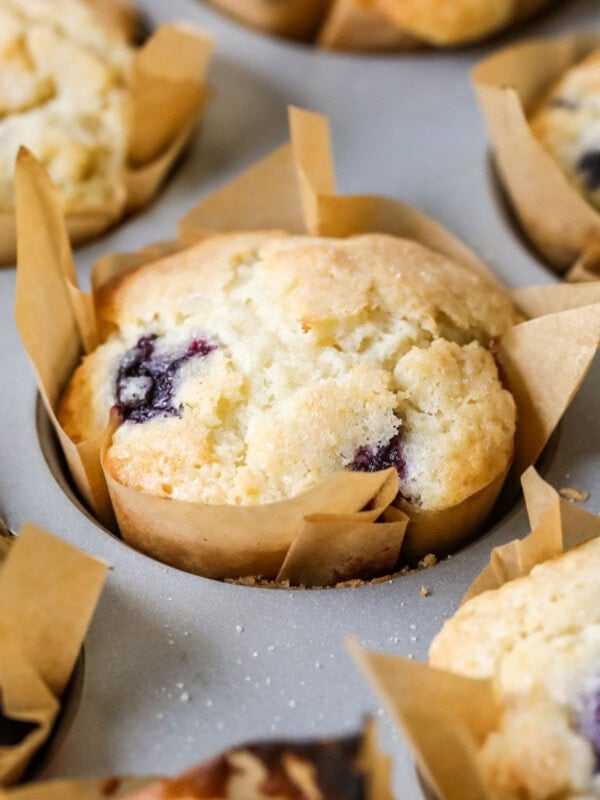 Sourdough blueberry muffins in parchment liners in a baking pan.