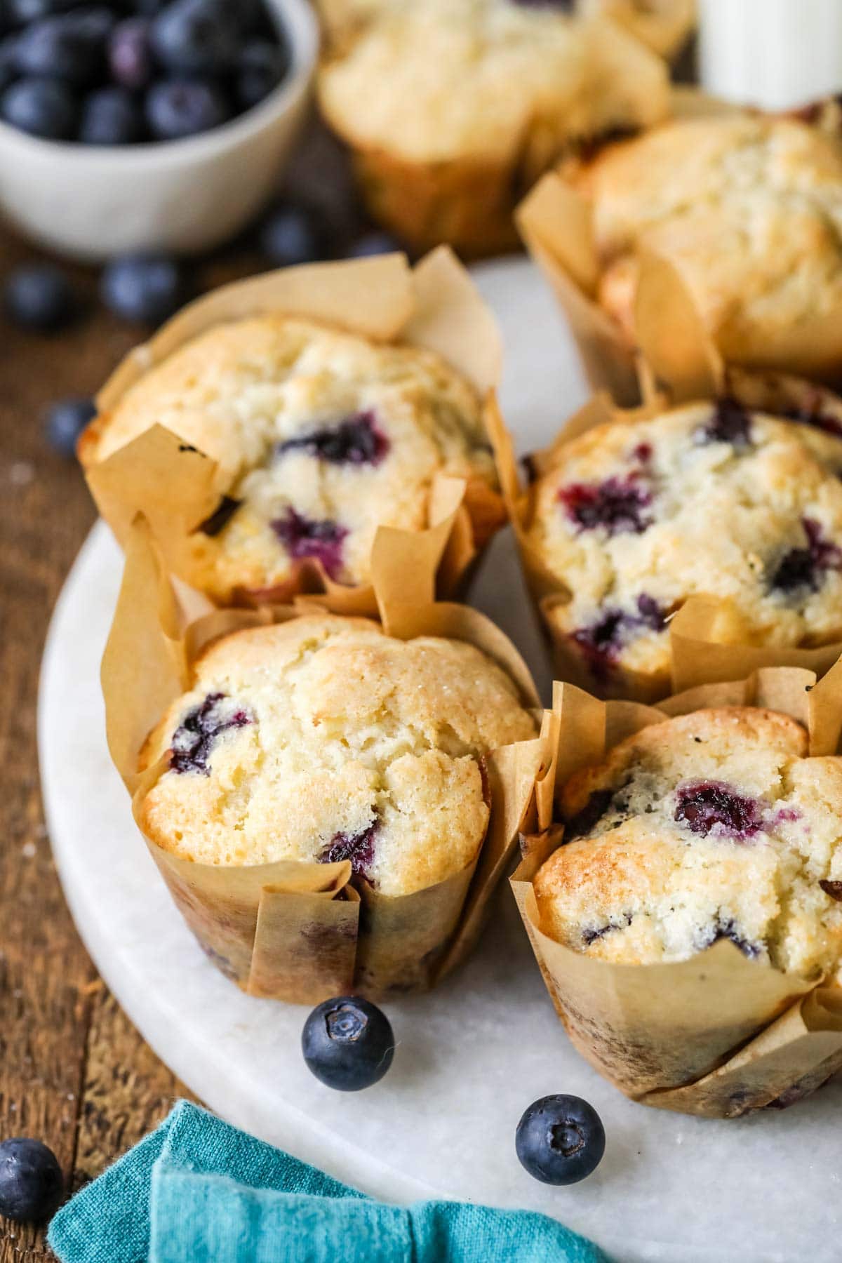 White plate of sourdough blueberry muffins in brown parchment wrappers.