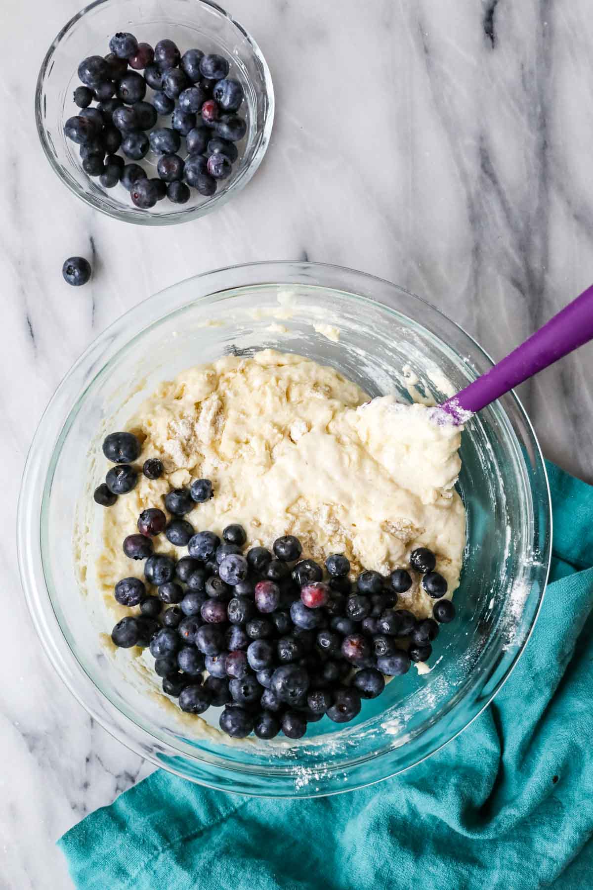 Overhead view of a bowl of muffin batter with blueberries scattered overtop.