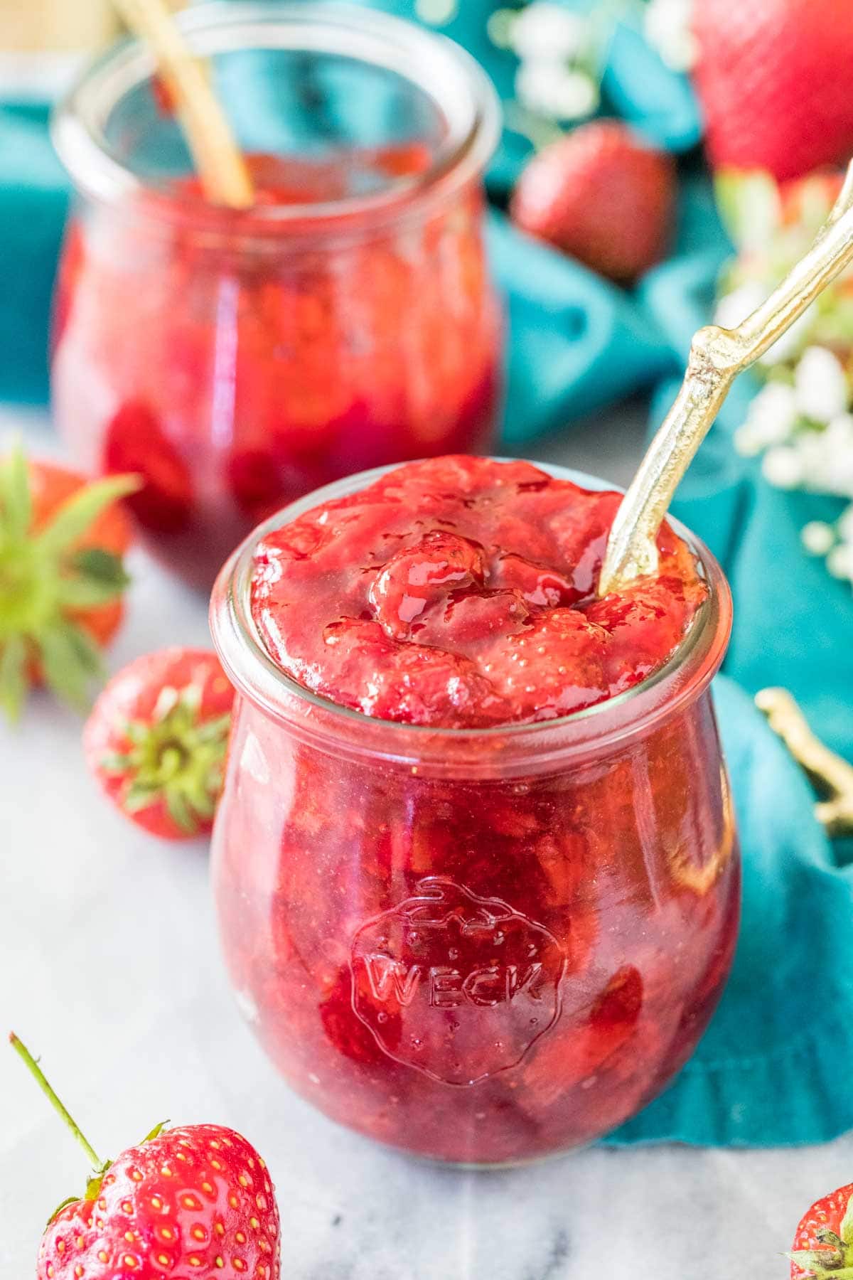 Jar of homemade strawberry sauce with a gold spoon sticking out of it.