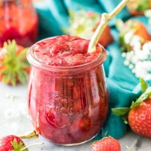 Jar of homemade strawberry sauce with a gold spoon sticking out of it.