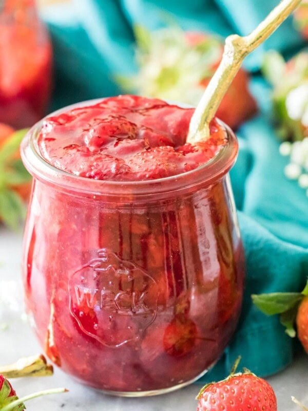 Jar of homemade strawberry sauce with a gold spoon sticking out of it.