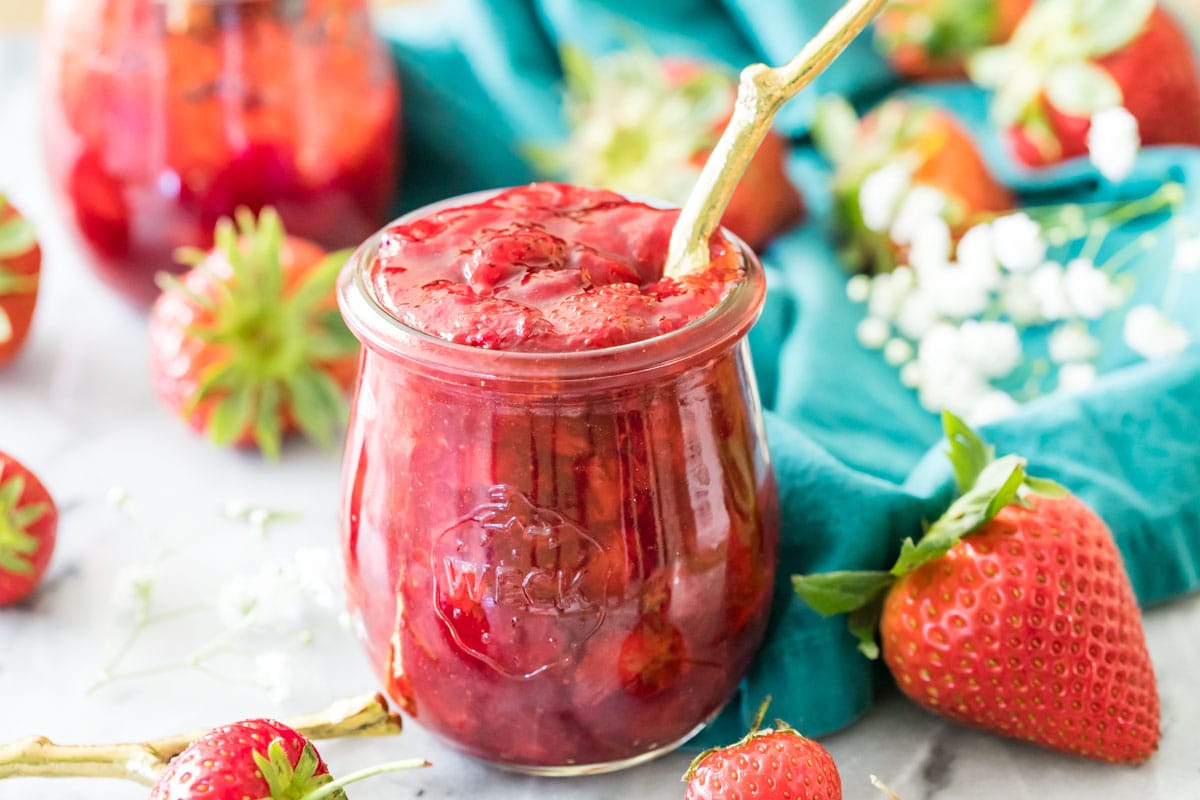 Jar of homemade strawberry sauce with a gold spoon sticking out of it.
