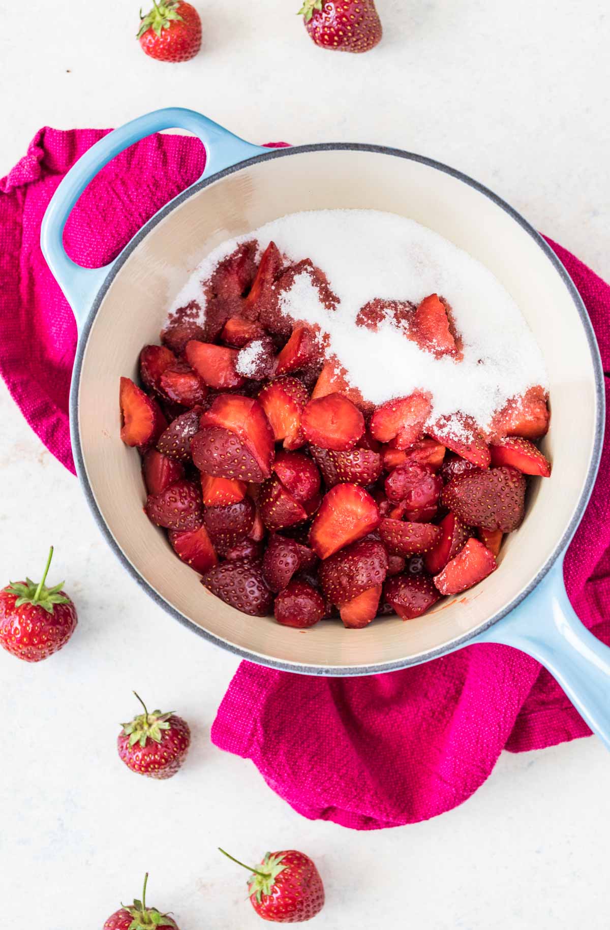 Overhead view of strawberries and sugar in a saucepan.