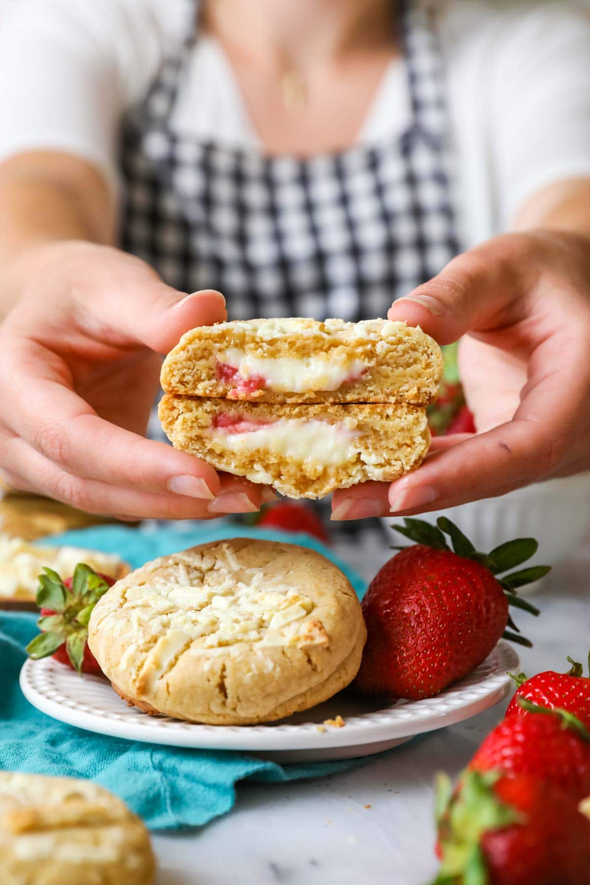 Hands holding two halves of strawberry cheesecake cookies with the cream cheese centers pointed towards the camera.