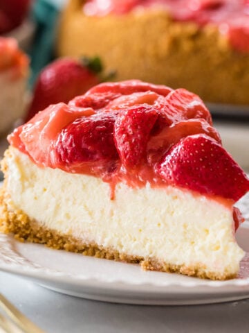 Slice of strawberry cheesecake on a plate with more cheesecake in the background.