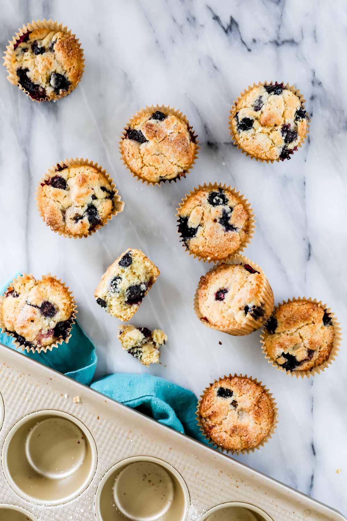 Overhead of blueberry muffin cut in half surrounded by intact muffins. The crumb appears dry and like cornbread